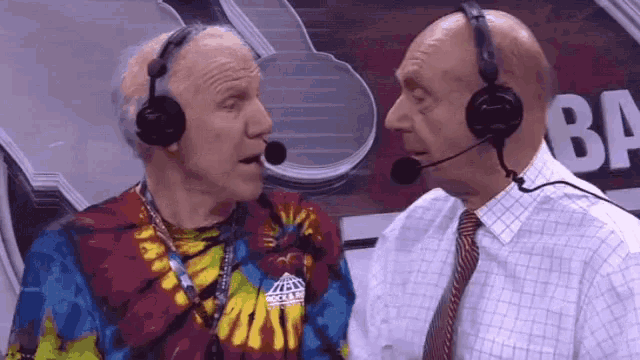 two men wearing headphones are talking to each other in front of a sign that says ba