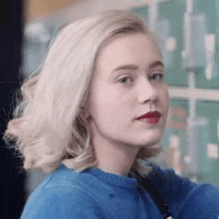 a blonde woman wearing a blue sweater and red lipstick is looking at the camera .