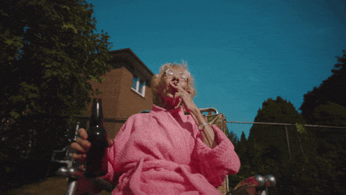an elderly woman in a pink robe is smoking a cigarette and holding a bottle of beer