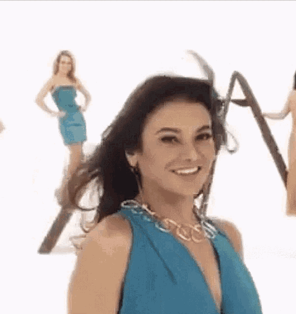 a woman in a blue dress and necklace is smiling while standing in front of a white background .