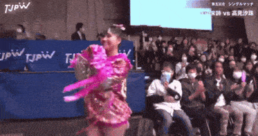 a woman in a pink dress is dancing in front of a crowd with tjpw written on the back
