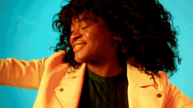 a woman with curly hair is wearing a yellow jacket and dancing with her eyes closed .