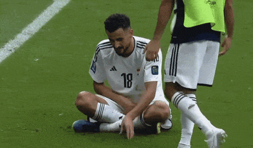 a soccer player with the number 18 on his jersey is sitting on the ground
