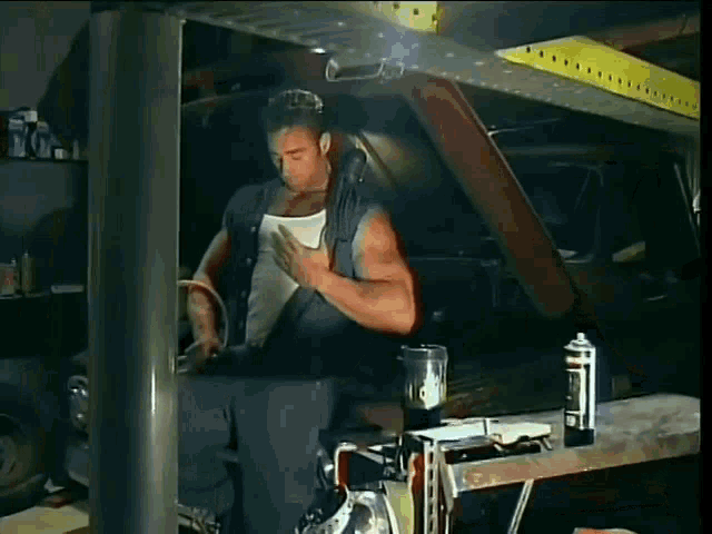 a man is working on a car in a garage with a blender and a spray can .