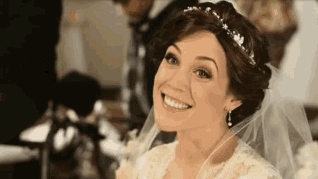 a bride in a wedding dress and veil is smiling and looking at the camera .