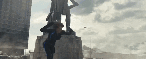 a woman in a black suit is standing next to a statue of a man .