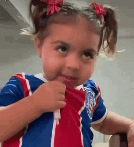 a little girl wearing a red , white and blue shirt is making a face .