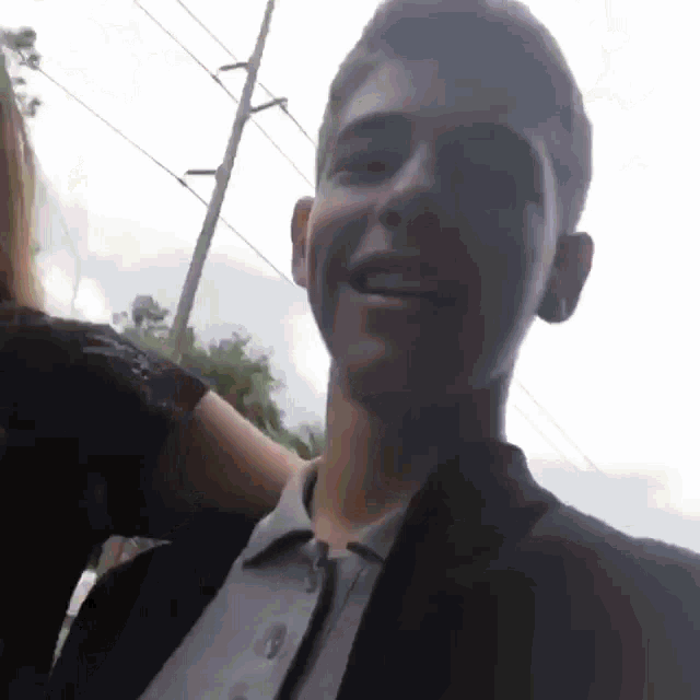a young man in a suit smiles while a woman holds his arm