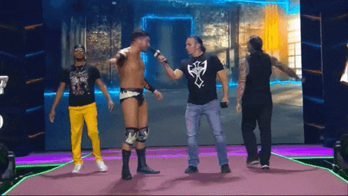 a man in a black shirt with a cross on it is talking to a wrestler