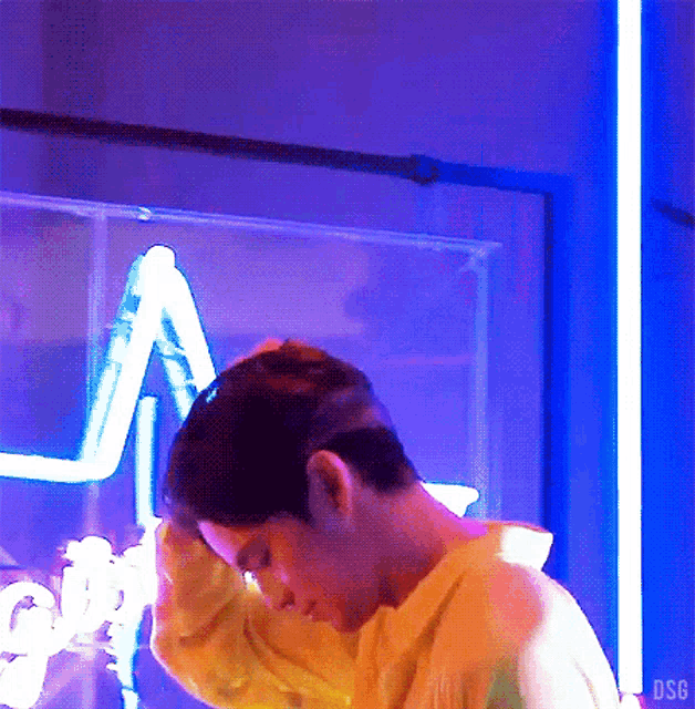 a man in a yellow shirt is standing in front of a neon sign that says dsf