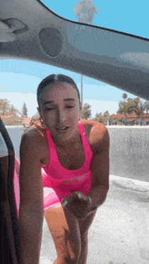 a woman in a pink tank top and shorts is standing in the back of a car