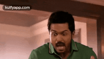 a man in a green shirt is making a funny face while standing in a room .