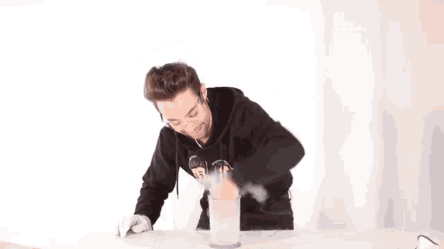 a man in a black hoodie is pouring liquid into a cup