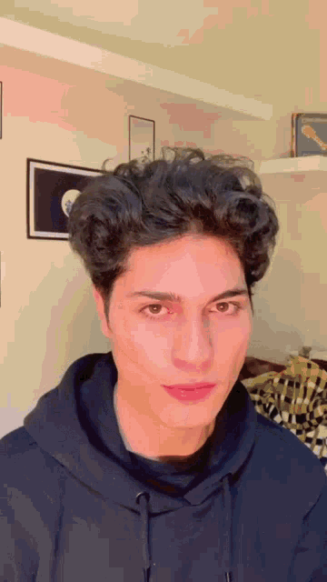 a young man with curly hair is wearing a black hoodie and making a funny face .