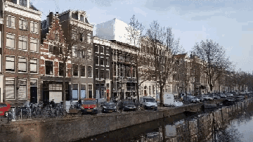 a row of buildings next to a river with cars parked on the sidewalk