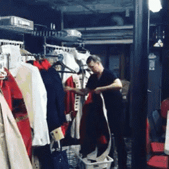 a man in a black shirt is standing in a room with clothes hanging on racks