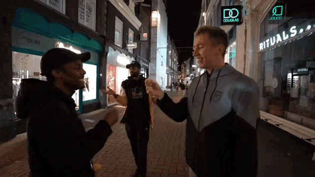 a man in a rituals sweatshirt talks to another man