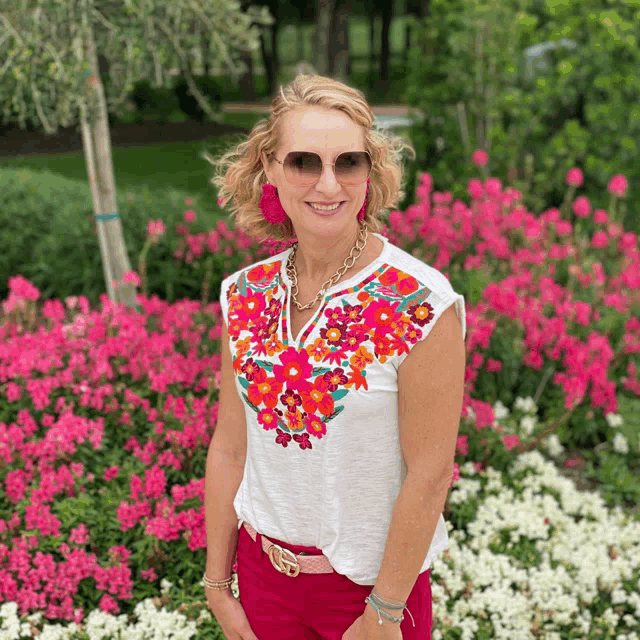 a woman wearing sunglasses and a white top with pink and orange flowers on it