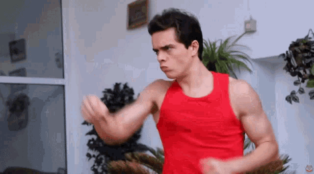 a man in a red tank top is standing in front of a plant