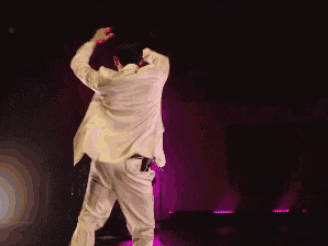 a man in a suit is dancing on a stage with purple lights behind him