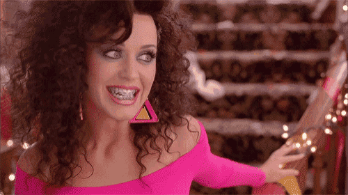 a woman with curly hair is wearing a pink top and earrings