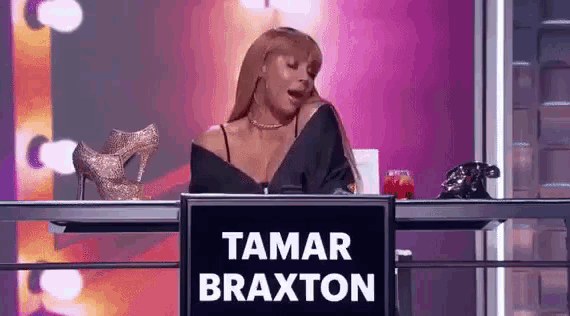 a woman is sitting at a desk with a sign that says tamar braxton on it .