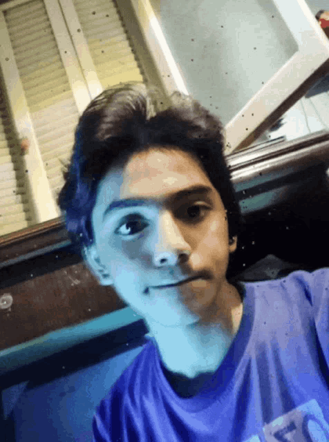 a young man wearing a blue shirt with the letter t on it takes a selfie