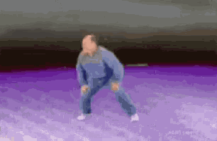 a man in a blue jacket and jeans is dancing in the snow .