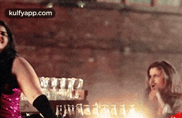 a woman in a pink dress is dancing in front of a bar filled with glasses .