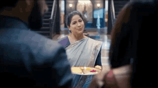 a woman in a saree is holding a plate of food in front of a man and a woman .