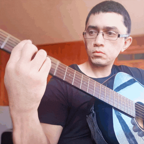 a man wearing glasses holds a blue guitar