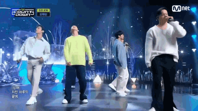 a group of men are singing and dancing on a stage with a mnet sign in the background .