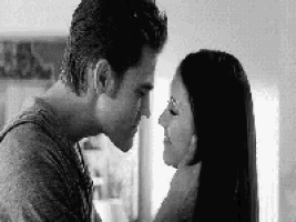 a black and white photo of a man and a woman kissing .