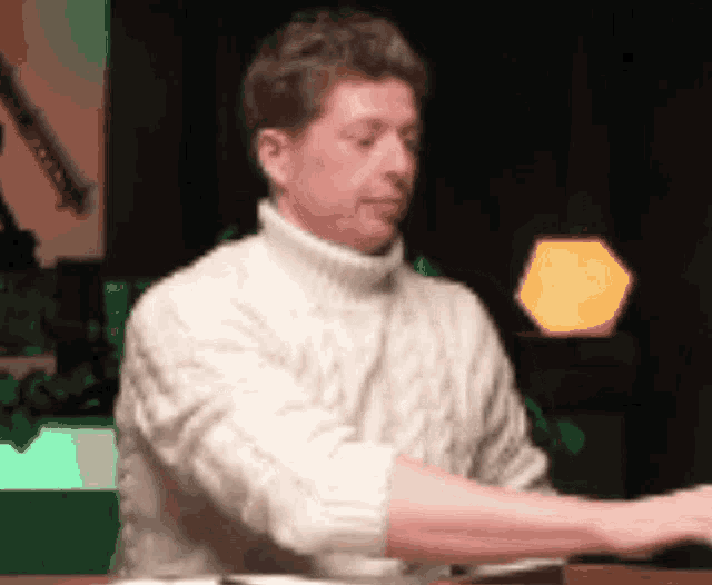 a man in a white sweater is sitting at a table with his arms crossed .