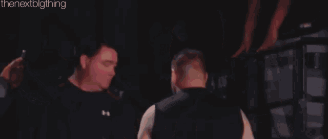 a man in a black tank top is standing in a dark room with other men .