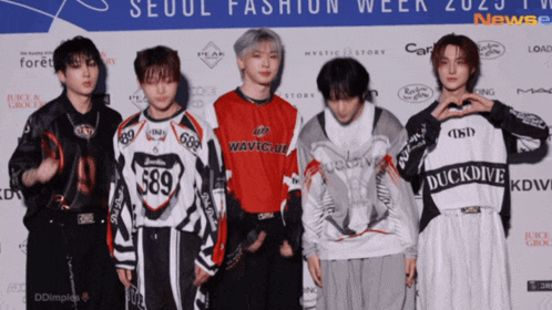 a group of young men are standing in front of a wall that says seoul fashion week