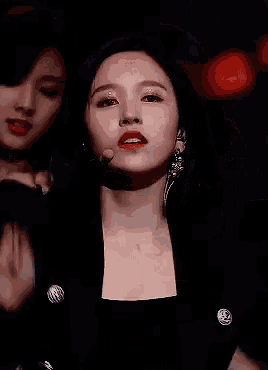 a woman in a black jacket and earrings is standing in front of a microphone .