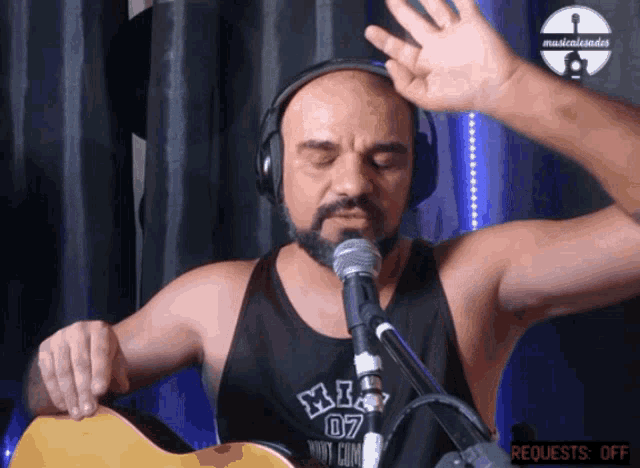 a man wearing headphones and a shirt that says xl 07 is playing a guitar