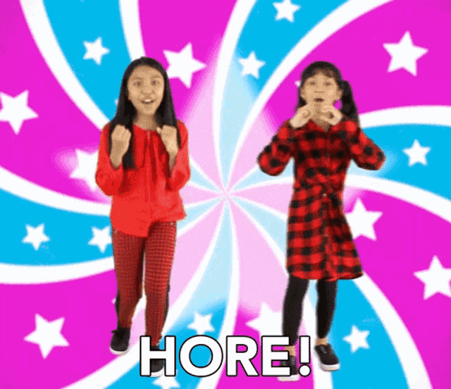 two young girls are dancing in front of a swirl and the words " here " are on the bottom right
