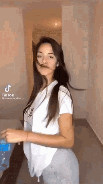 a woman in a white shirt is dancing in a room with her hair blowing in the wind .