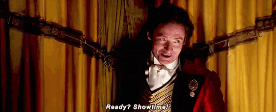 a man in a circus costume is standing in front of a yellow curtain and asking ready ? showtime .