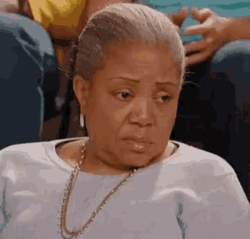 a woman wearing a necklace and earrings is sitting in a chair making a funny face .