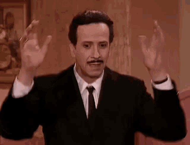 a man in a suit and tie is making a funny face with his hands in the air .