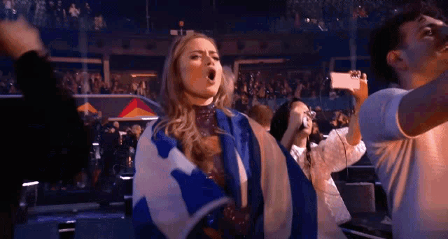 a woman is holding a greek flag while a man takes a picture of her .