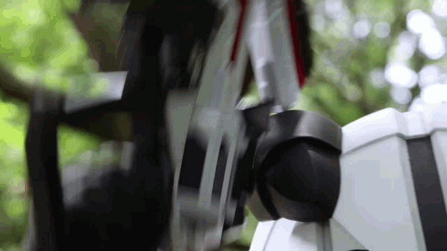 a close up of a robot 's arm with a blurry background of trees