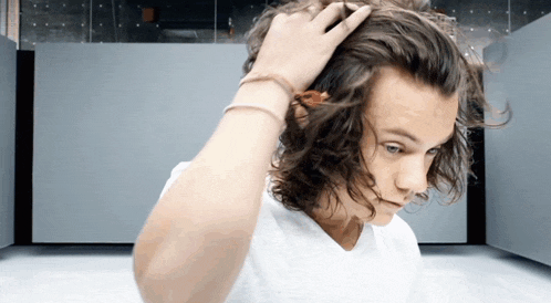a young man with long curly hair is touching his head