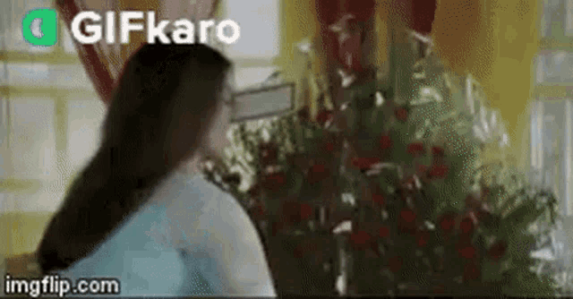 a woman with long hair is standing in front of a christmas tree in a room .