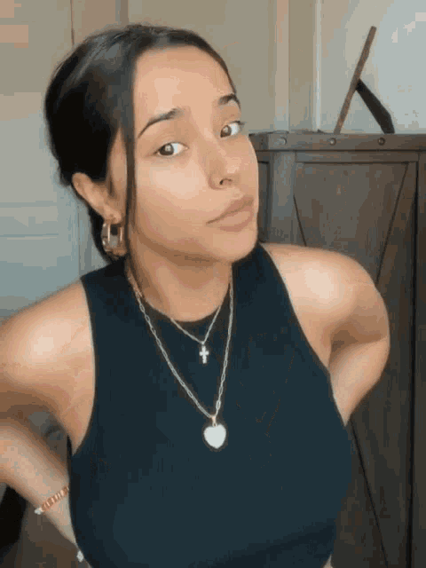 a woman wearing a black tank top and a necklace with a heart on it