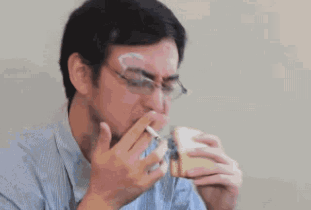 a man eating a sandwich with two cigarettes sticking out of his nose