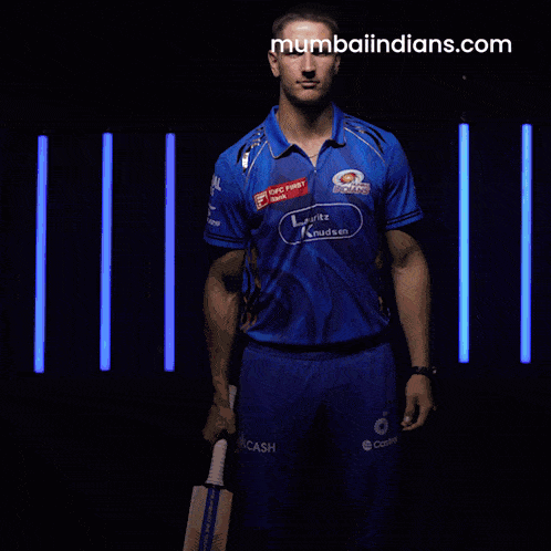a man in a blue shirt holding a cricket bat with mumbaiindians.com written on the bottom